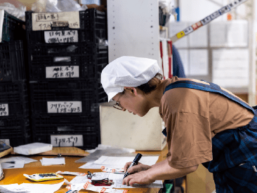 帽子を着用した作業員が帳票を確認している。